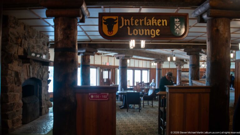 Interlaken Lounge sign with heraldic shields above a log-columned seating area and stone fireplace.