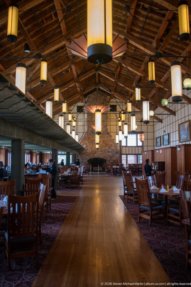 Central aisle through the dining room toward a stone fireplace, with hanging lanterns and tables on both sides.