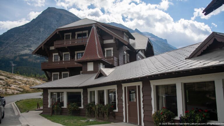 Brown multi-story lodge wing with balconies, white-trimmed windows, and mountains rising behind it.