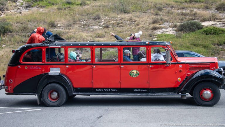 Red Glacier National Park touring bus with passengers and roof luggage parked beside the lodge.