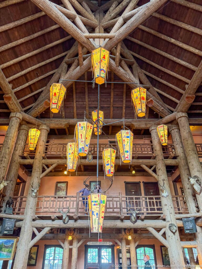 Colorful hanging lanterns suspended among massive log beams and trusses above the multi-story Great Room.