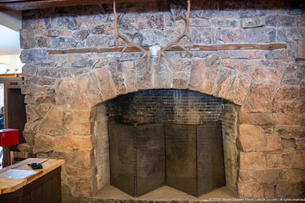 Large stone fireplace with arched firebox, metal mesh screen, and mounted antlers above the opening.