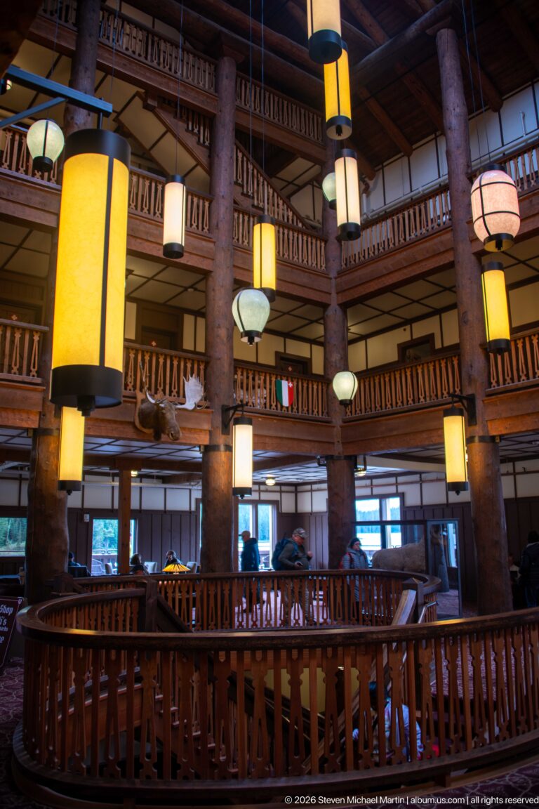 Large glowing lanterns suspended among log columns and multiple wooden balcony levels in the Great Room.