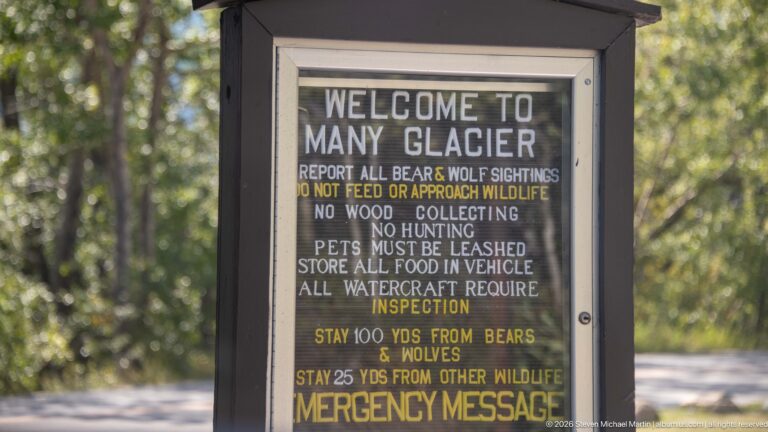 Welcome to Many Glacier sign listing wildlife safety, food storage, leash, hunting, and distance regulations.