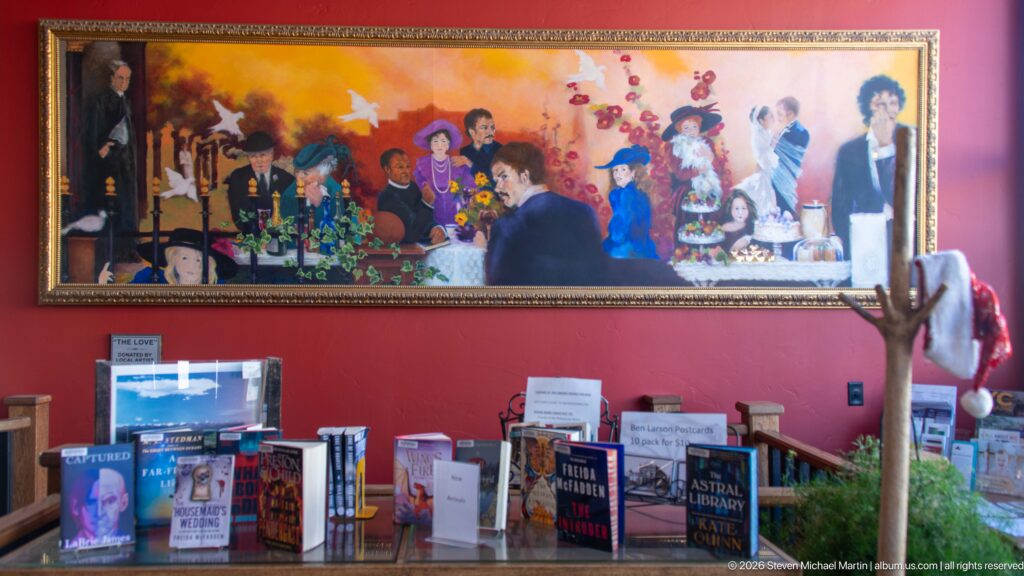 Large colorful figurative painting above a table of displayed books inside the Philipsburg Public Library.