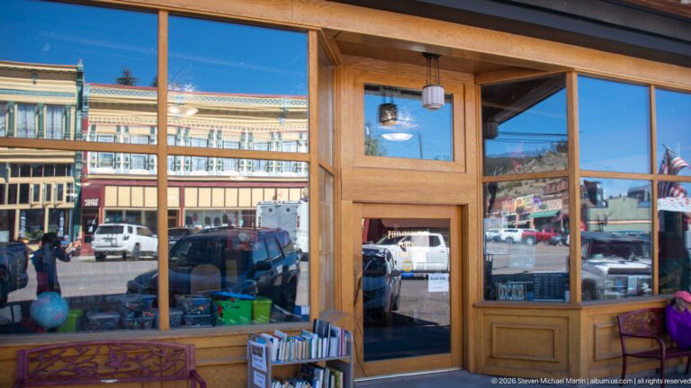 Wood-framed shop entrance reflecting the ornate Walker Commercial Company building, parked vehicles, and pedestrians across the street.