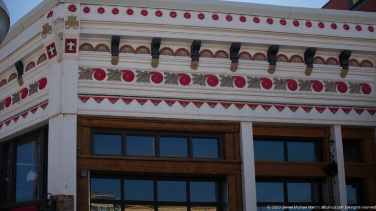 Close view of the J.C. McLeod Building’s cream, red, and dark-green frieze with circular motifs, brackets, and patterned trim.