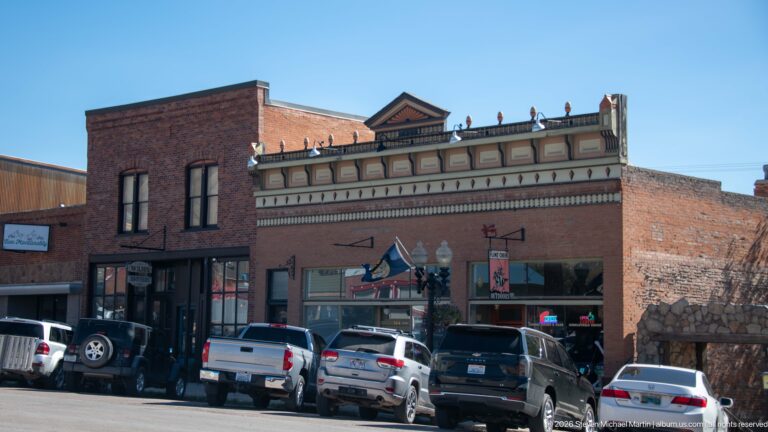 Historic J.C. McLeod Building with ornate painted cornice, central pediment, broad storefront windows, and parked vehicles along the curb.