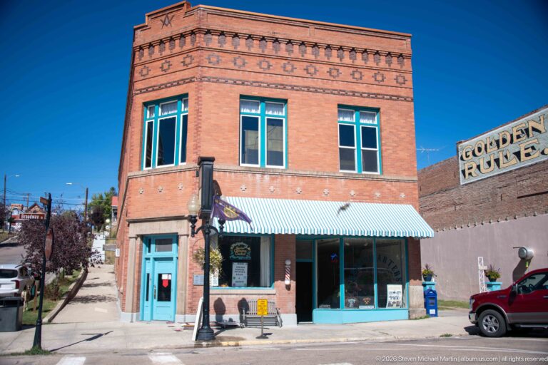 Two-story brick corner storefront with blue-trimmed windows and striped awning beside a large painted GOLDEN RULE wall sign.