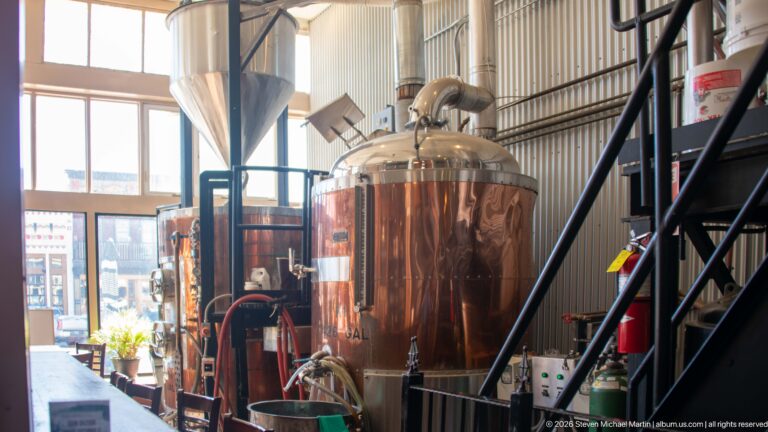 Copper-clad brewing tanks with stainless fittings, hoses, stairs, and industrial equipment inside Philipsburg Brewing Company.