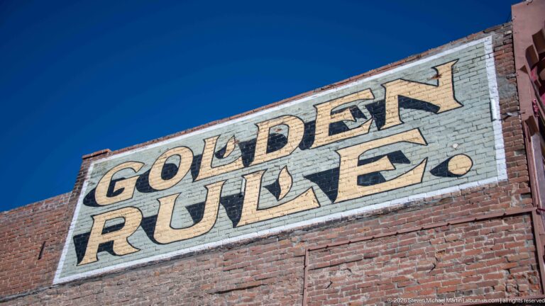Large weathered GOLDEN RULE ghost sign painted across a red-brick wall beneath a deep blue sky.
