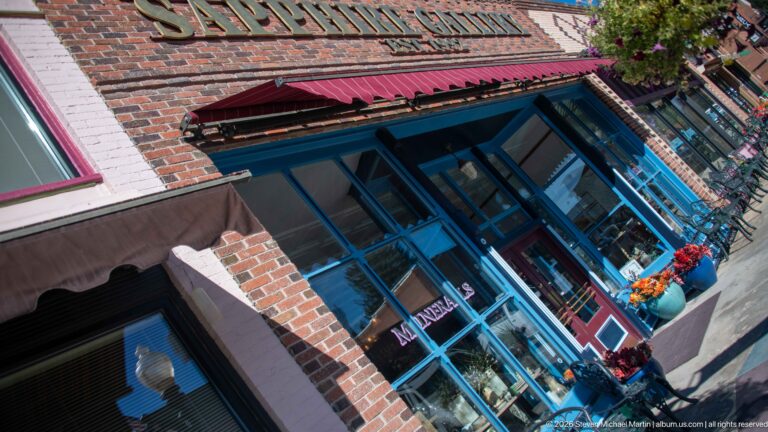 Oblique view of the former C.T. Huffman Grocery building, now Sapphire Gallery, with blue storefront framing and red awnings.