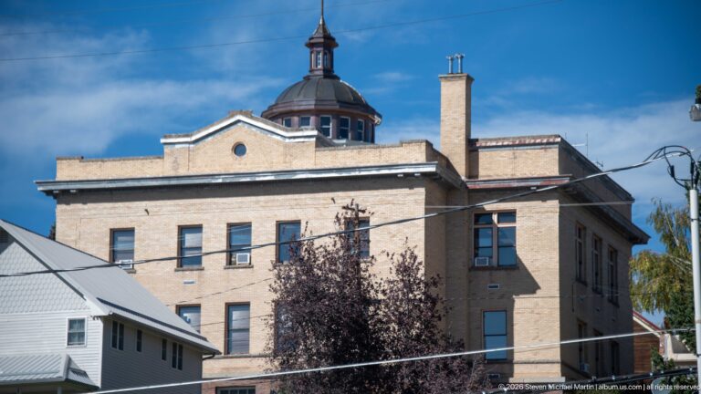Side view of the Granite County Courthouse with pale masonry walls, rows of windows, chimneys, and a domed central cupola.