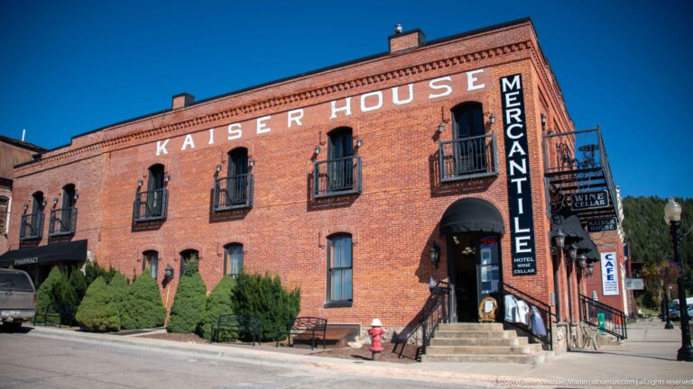 Kaiser House brick building with painted name, arched upper windows, iron balconies, corner entrance, and vertical MERCANTILE sign.
