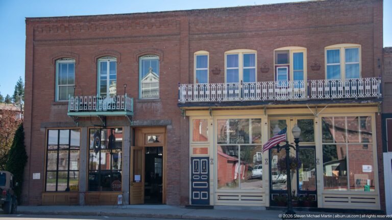 Closer view of the Weinstein Building with tall second-story windows, two iron balconies, decorative brickwork, and ground-floor storefronts.