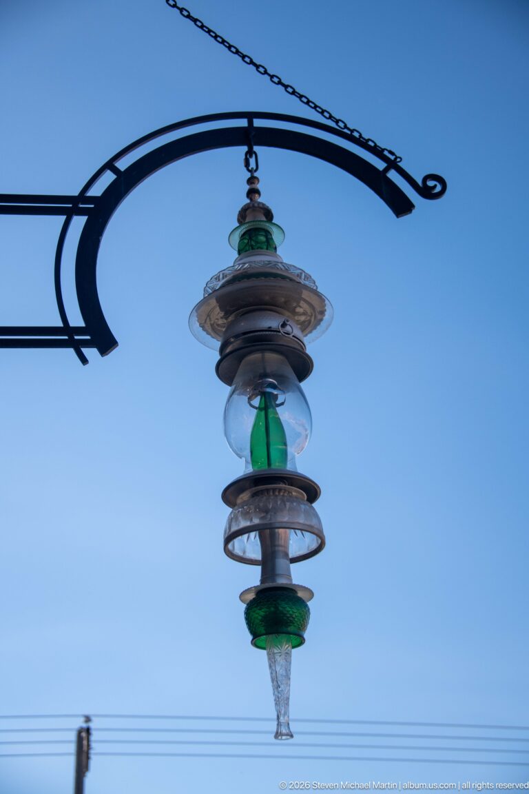 Decorative hanging streetlight with green glass, stacked metal shades, and pointed glass pendant suspended from a black bracket.