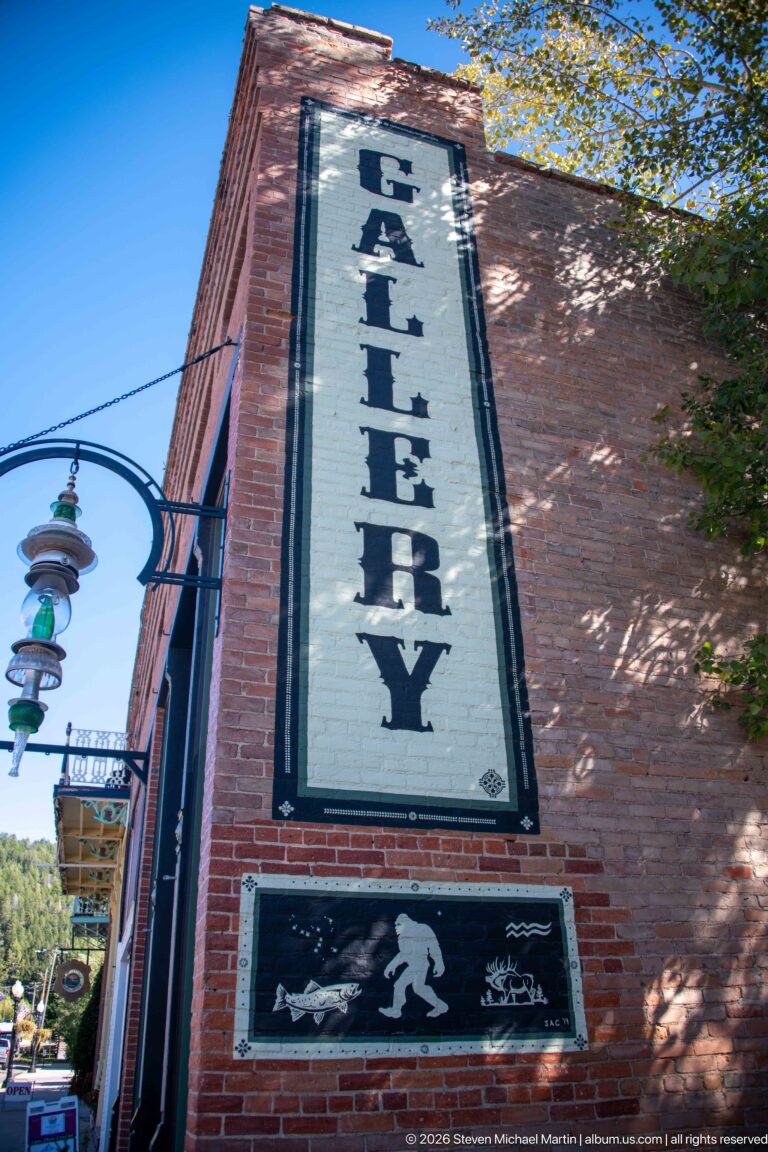 Large vertical ALLEYWAY sign painted on a red-brick wall above a black graphic panel and decorative street fixtures.