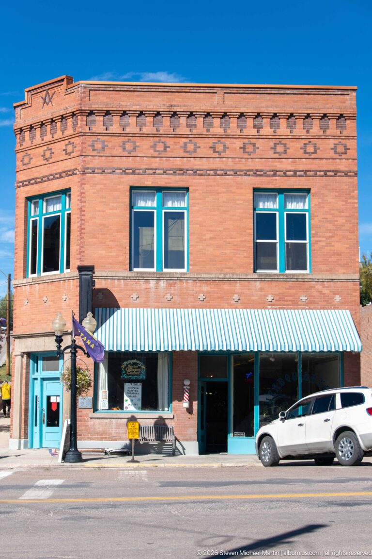 Two-story red-brick commercial building with corbelled cornice, upper windows, striped awning, and ground-floor storefronts.