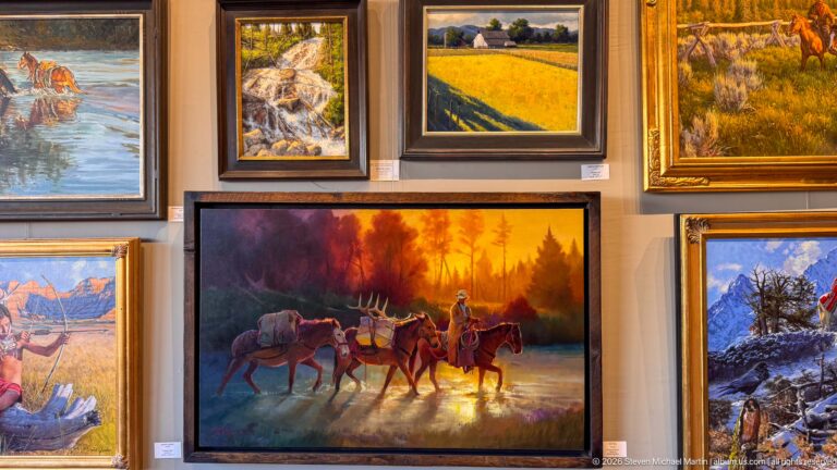 Gallery wall filled with framed western paintings, centered on pack animals and riders moving through warm forest light.