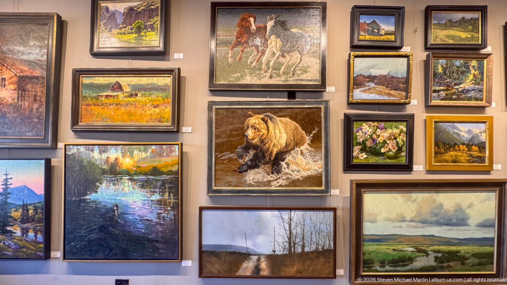 Gallery wall with framed paintings of a bear, horses, mountains, flowers, waterways, and western landscapes.