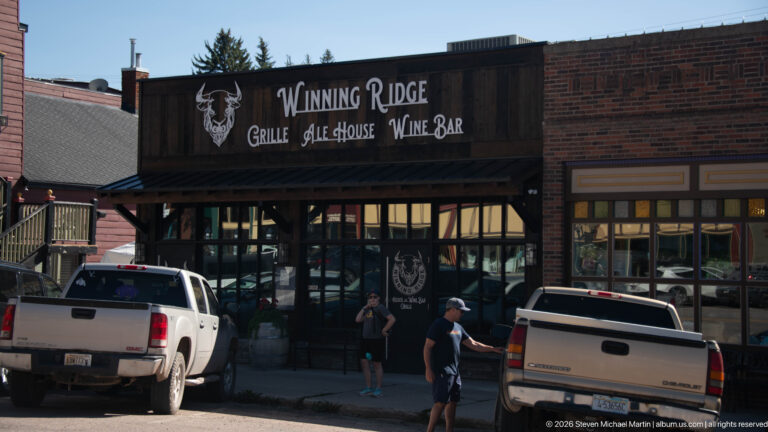 Winning Ridge Grille, Ale House and Wine Bar storefront with dark wood signboard, broad windows, pedestrians, and pickup trucks.