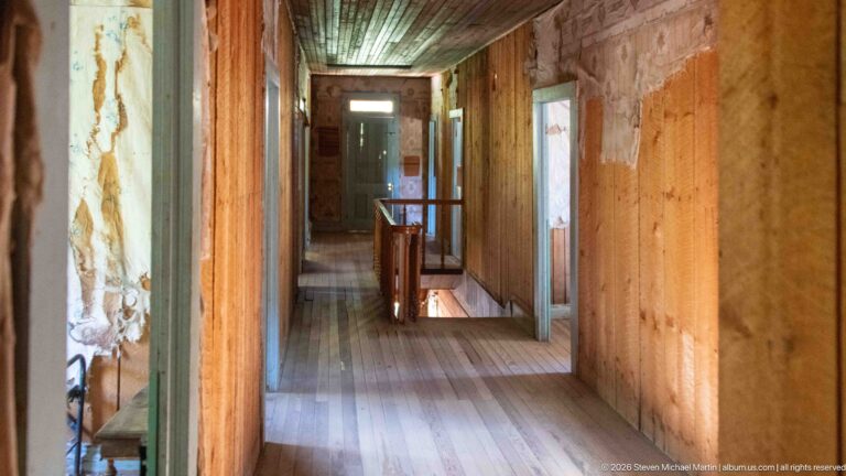 Narrow wooden hallway with plank floor, open doorways, stair railing, and worn wall finishes inside a historic Garnet building.