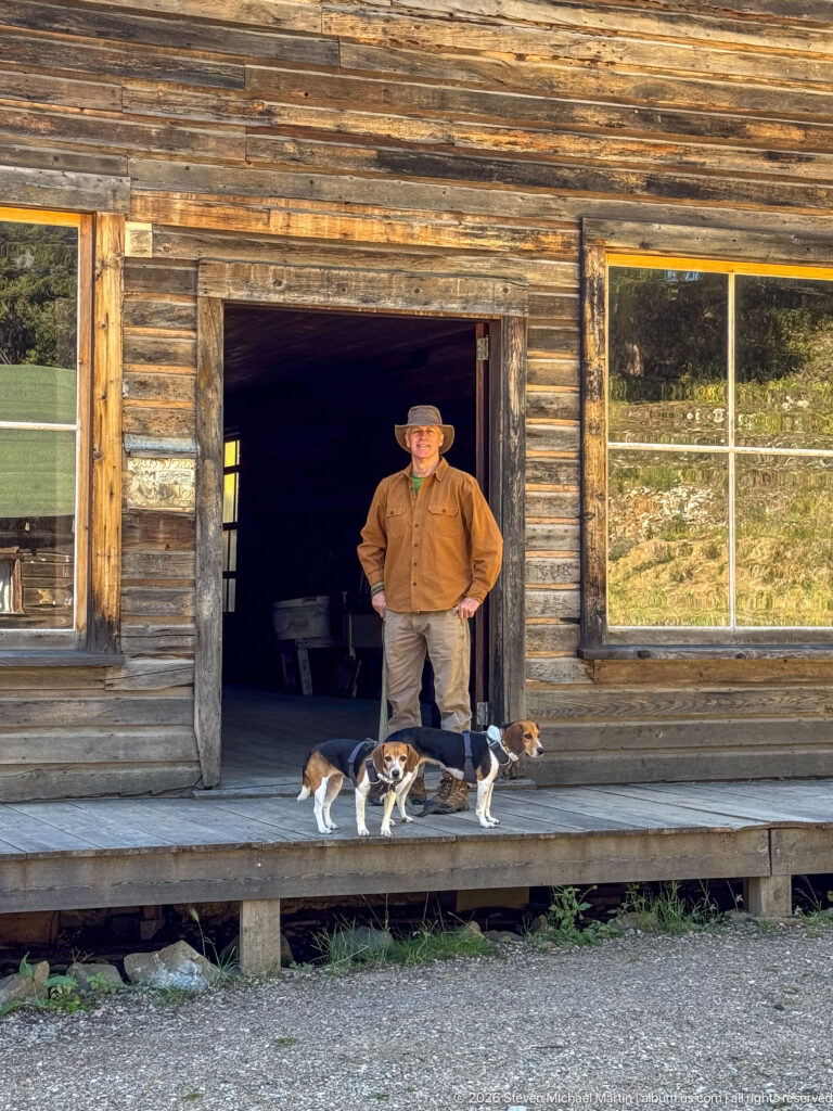 Visitor standing in the doorway of a weathered false-front storefront with two beagles on the porch and large windows on both sides.