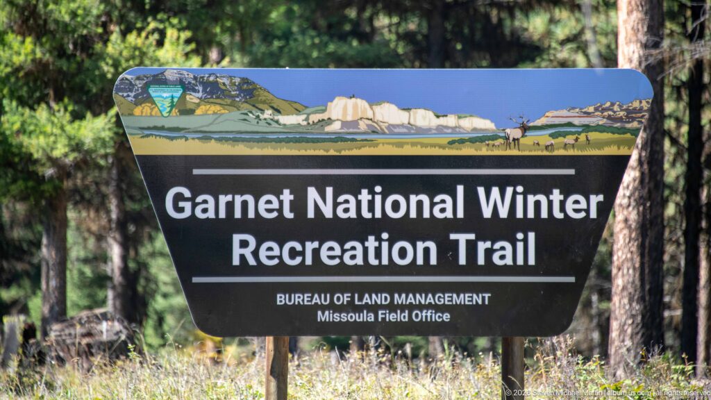 Large Garnet National Winter Recreation Trail sign for the Bureau of Land Management Missoula Field Office among conifers.