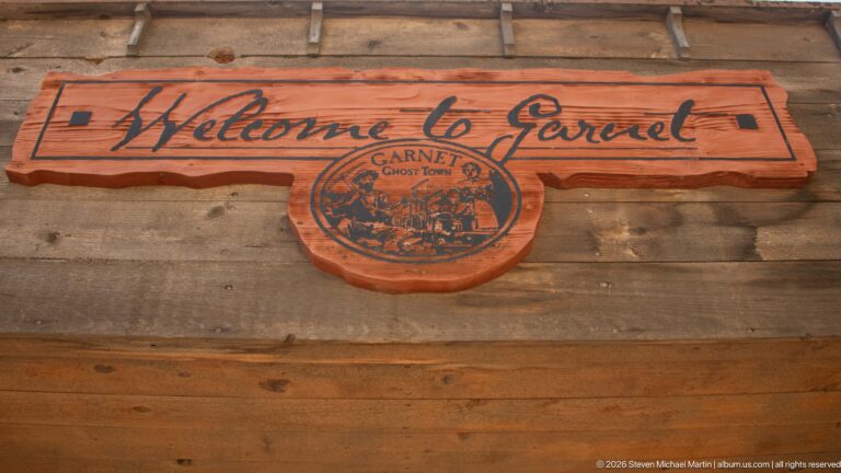 Carved reddish wooden sign reading Welcome to Garnet with a circular Garnet Ghost Town emblem below.