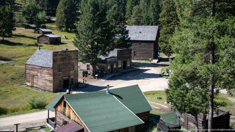 Elevated townsite view with Garnet’s false-front buildings, larger two-story structure, green-roofed visitor center, roads, and surrounding forest.