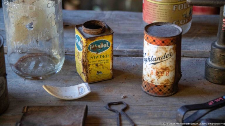 Yellow Global powder tin, Highlander cylindrical container, clear embossed bottle, and small metal vessels on a wooden surface.