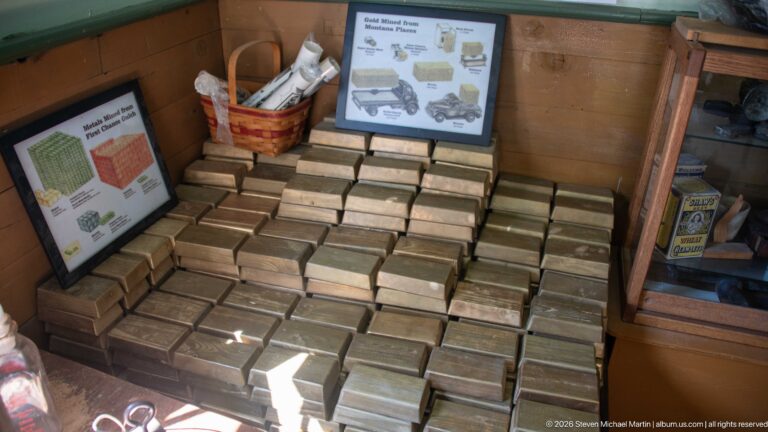 Large stack of small rectangular historic-style boxes arranged beneath two interpretive signs inside a wooden shop interior.