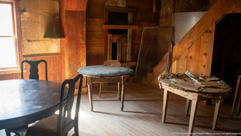 Wood-paneled historic room containing several tables and mismatched chairs, with sunlight entering from a window at left.