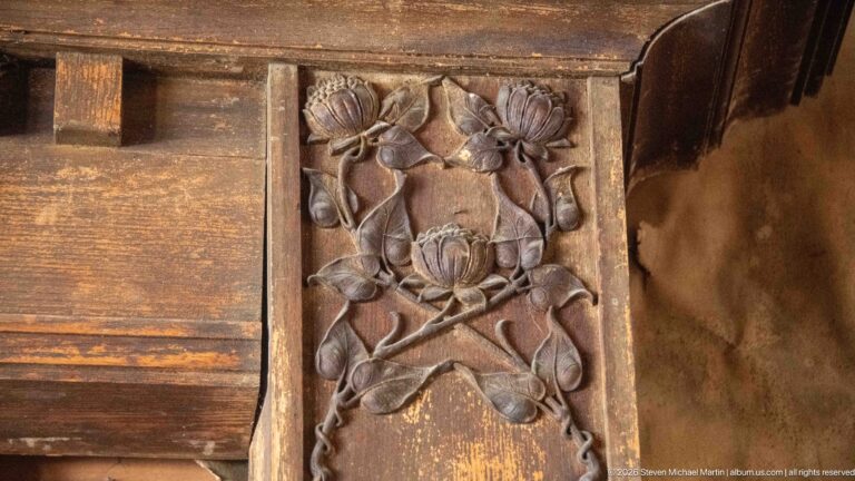 Close view of a dark wooden furniture panel carved in relief with flowers, leaves, stems, and scrolling forms.